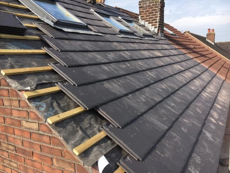 New grey roof tiles being laid over fresh battens and membrane on a brick house